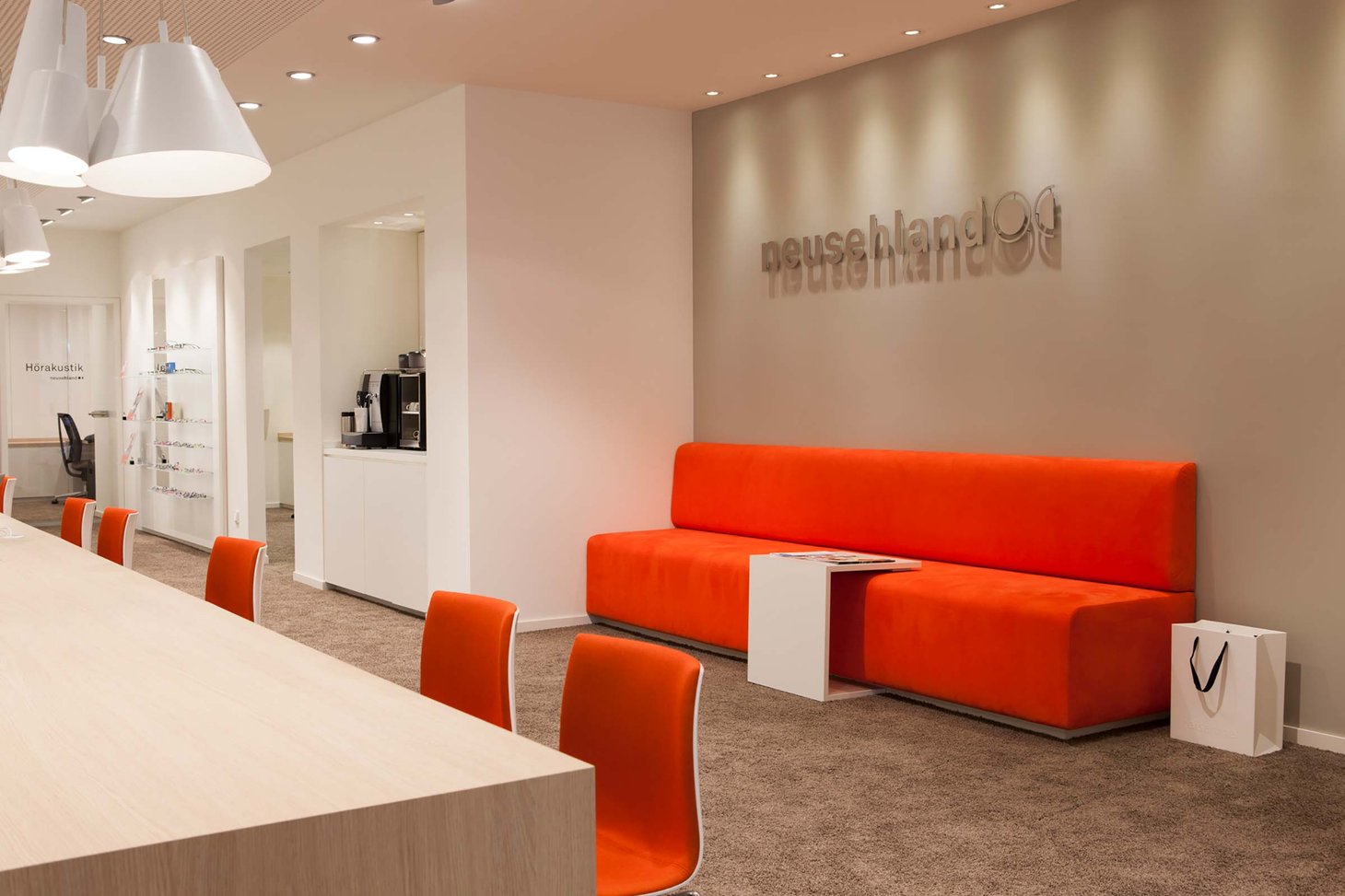 Wartebereich mit orangefarbenem Sofa und Stühlen, Schriftzug "neusehland" an der Wand