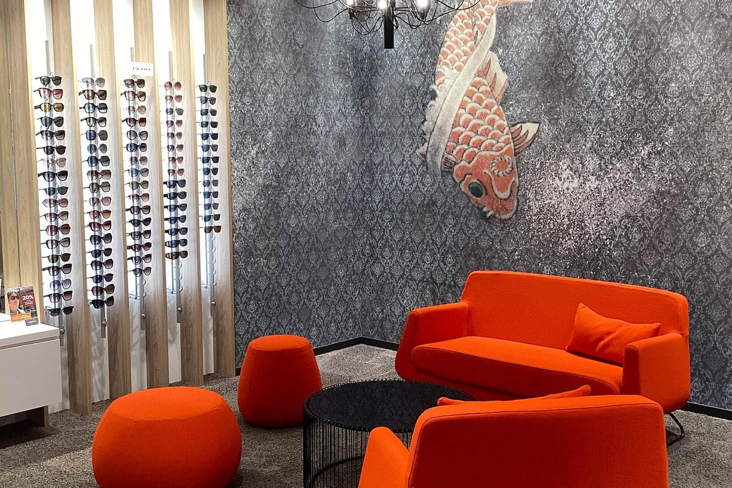 Wartebereich mit orangefarbenem Sofa, Koi-Wandbild und Brillenregal aus Holz
