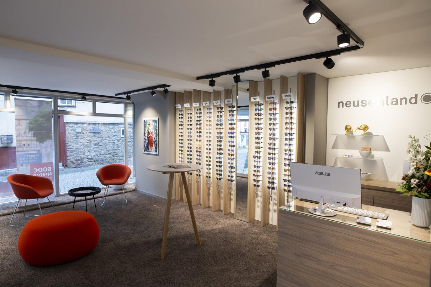 Optiker-Innenraum mit Sonnenbrillenständern, Empfangstresen und Schriftzug "neusehland"