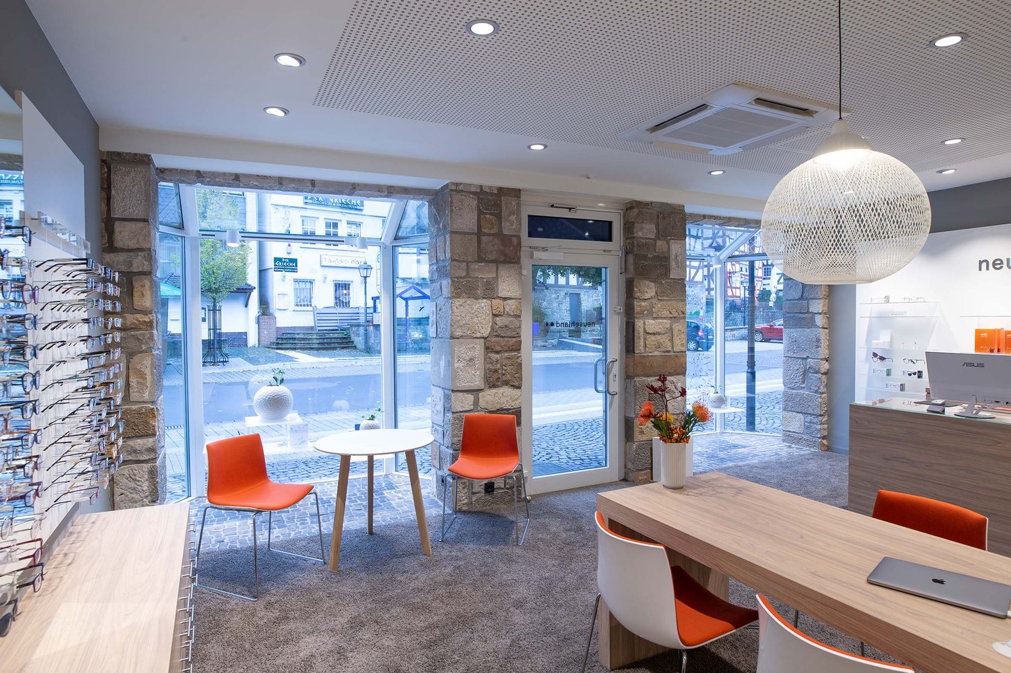 Wartebereich mit zwei orangefarbenen Stühlen und großem Schaufenster mit Natursteinrahmen