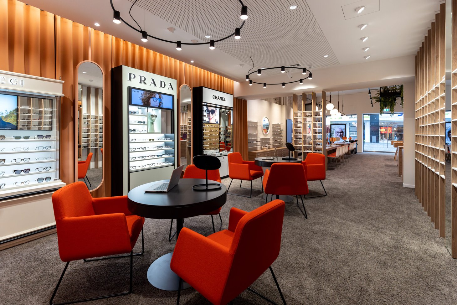 Wartebereich mit orangen Sesseln, Marken-Displays mit Aufschrift "PRADA" und "CHANEL"