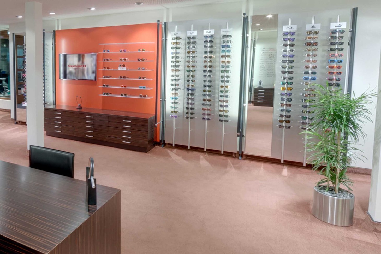 Sonnenbrillenausstellung an orangefarbener Wand mit Schubladen-Unterschrank