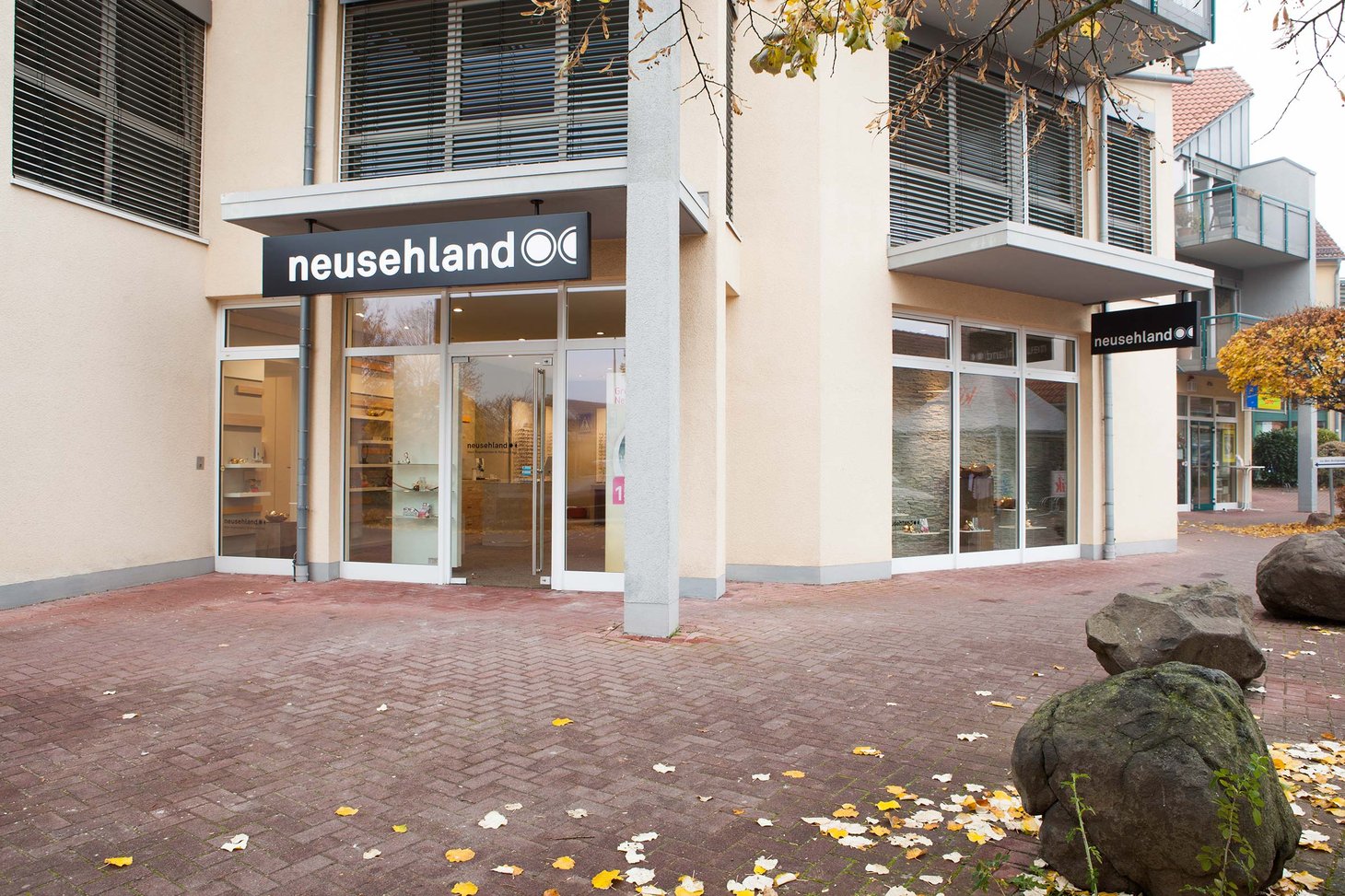 Ladenfront mit Schriftzug "neusehland" an einem Eckgebäude, Herbstlaub auf dem Pflasterboden