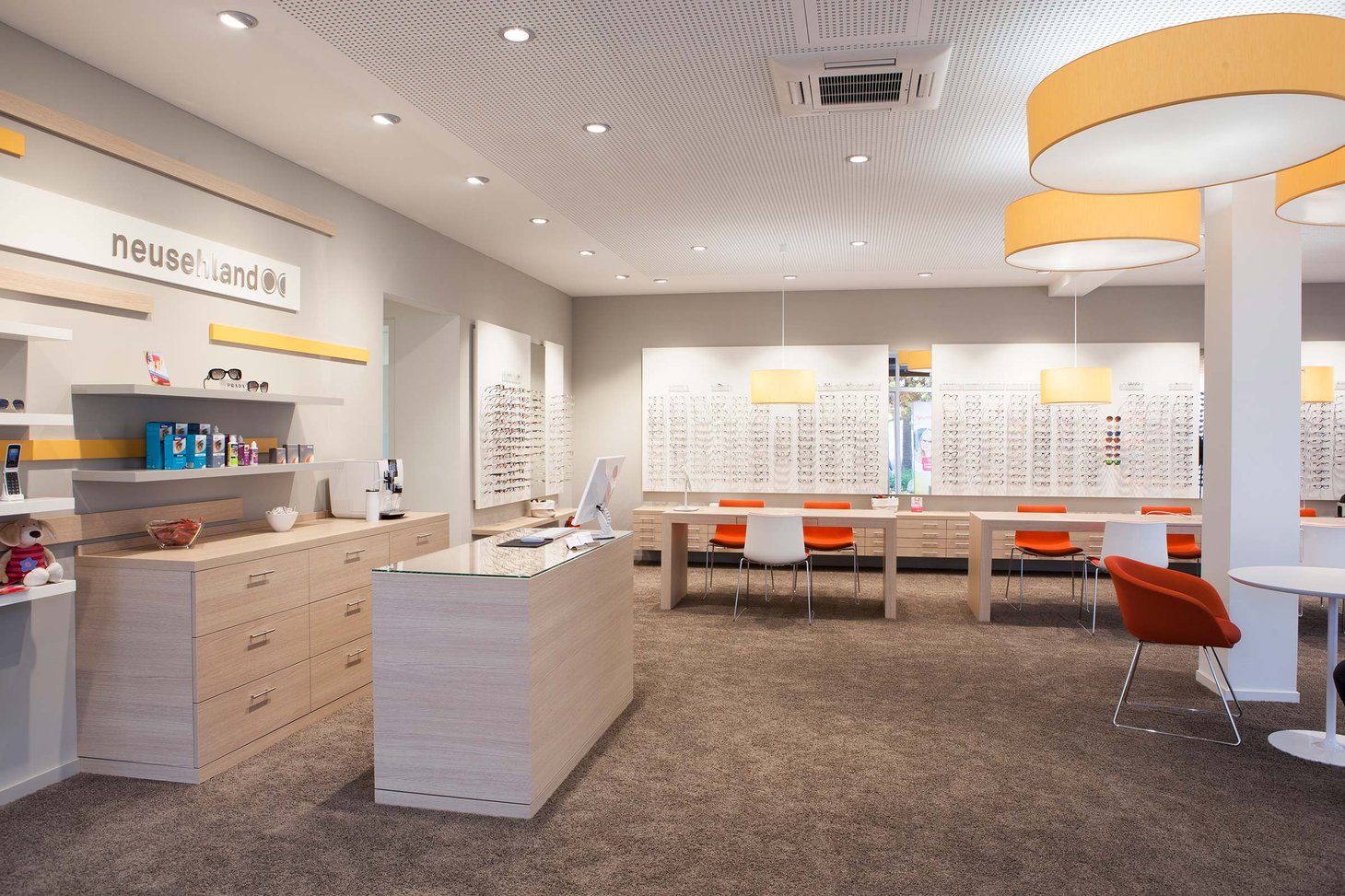 Empfangstheke eines Optikers mit großer Brillenwand im Hintergrund und Logo "neusehland"