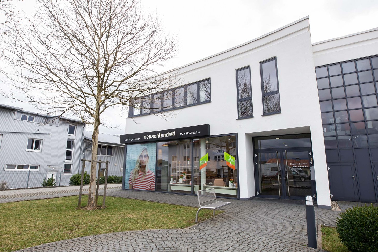 Weißes Flachdachgebäude mit Schriftzug "neusehland – Mein Augenoptiker Mein Hörakustiker"