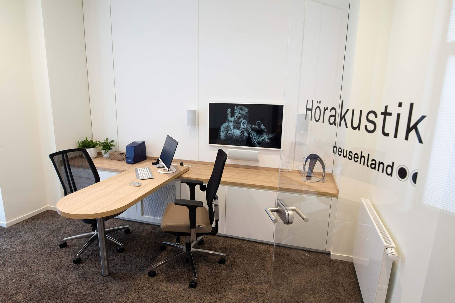 Hörakustik-Beratungsraum mit Schreibtisch, zwei Bildschirmen und Aufschrift "Hörakustik neusehland"