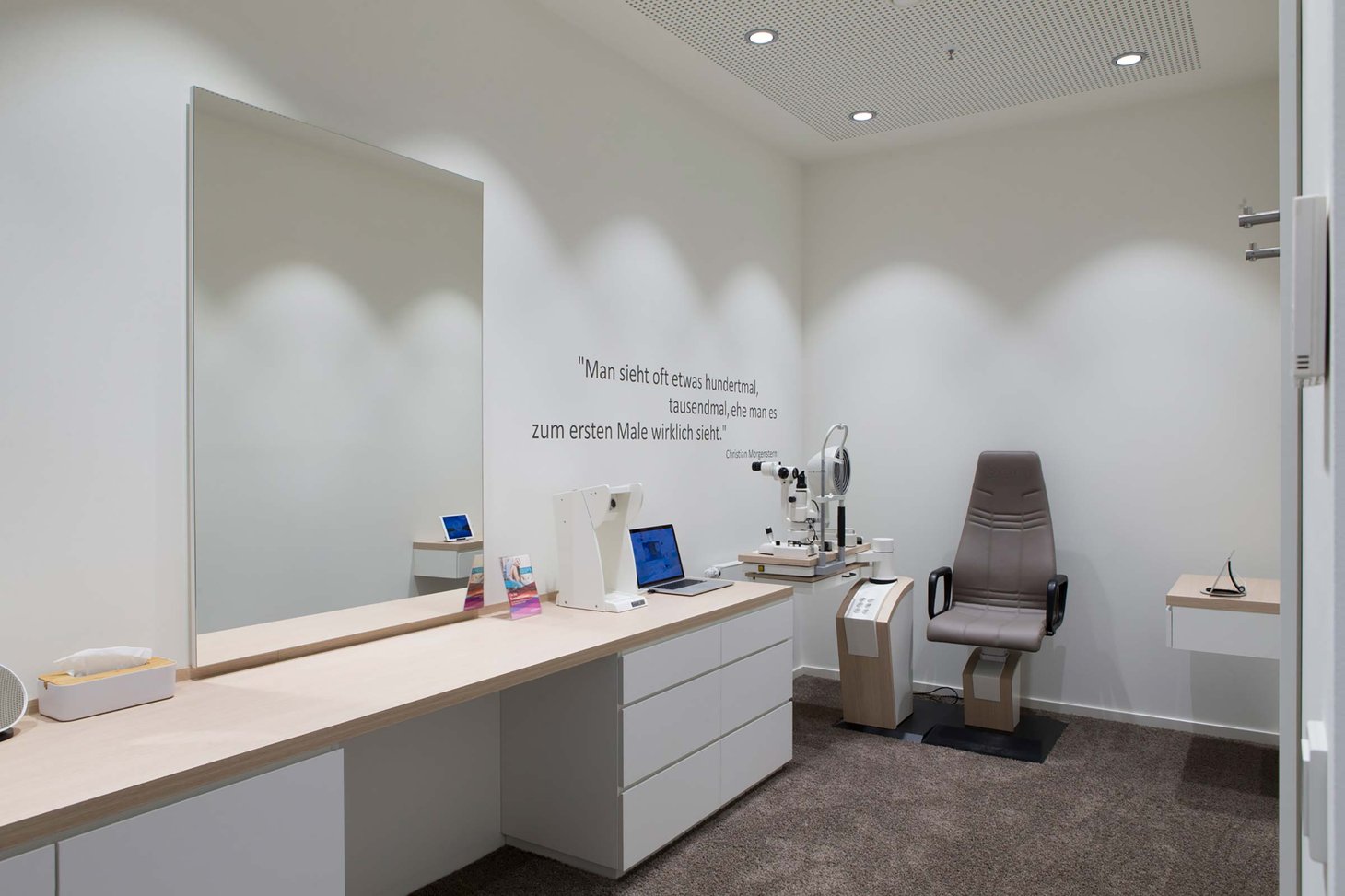 Augenoptik-Messraum mit Untersuchungsstuhl, Geräten und Zitat an der Wand, Waschbecken seitlich