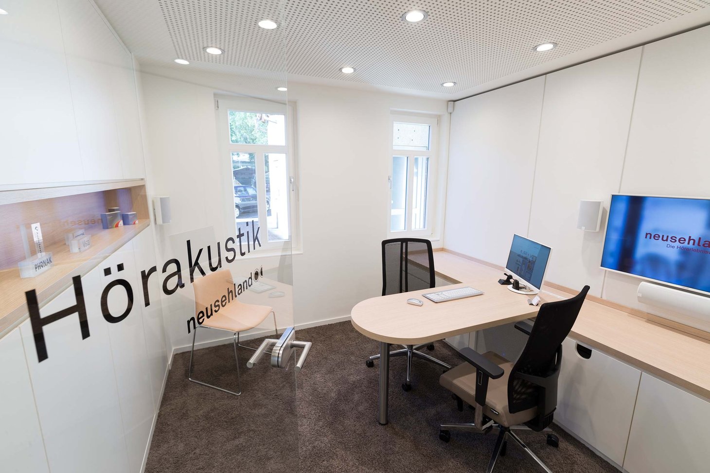 Hörakustik-Beratungsraum mit ovalem Tisch, zwei Bildschirmen und Aufschrift "Hörakustik neusehland"