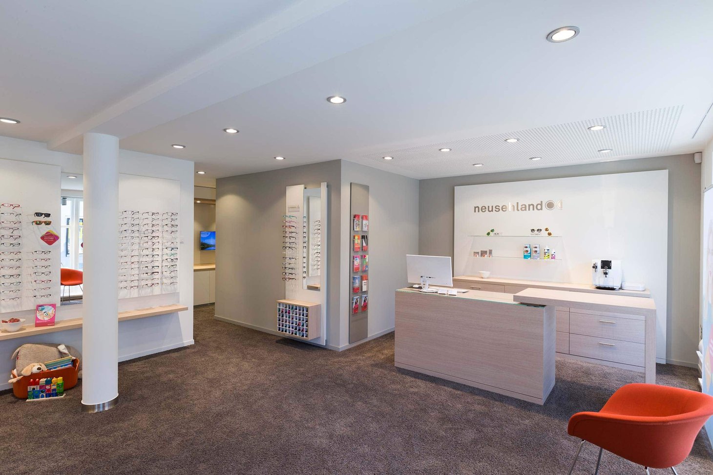Empfangsbereich eines Optikers mit Tresen, Brillenregalen und Logo "neusehland" an der Wand