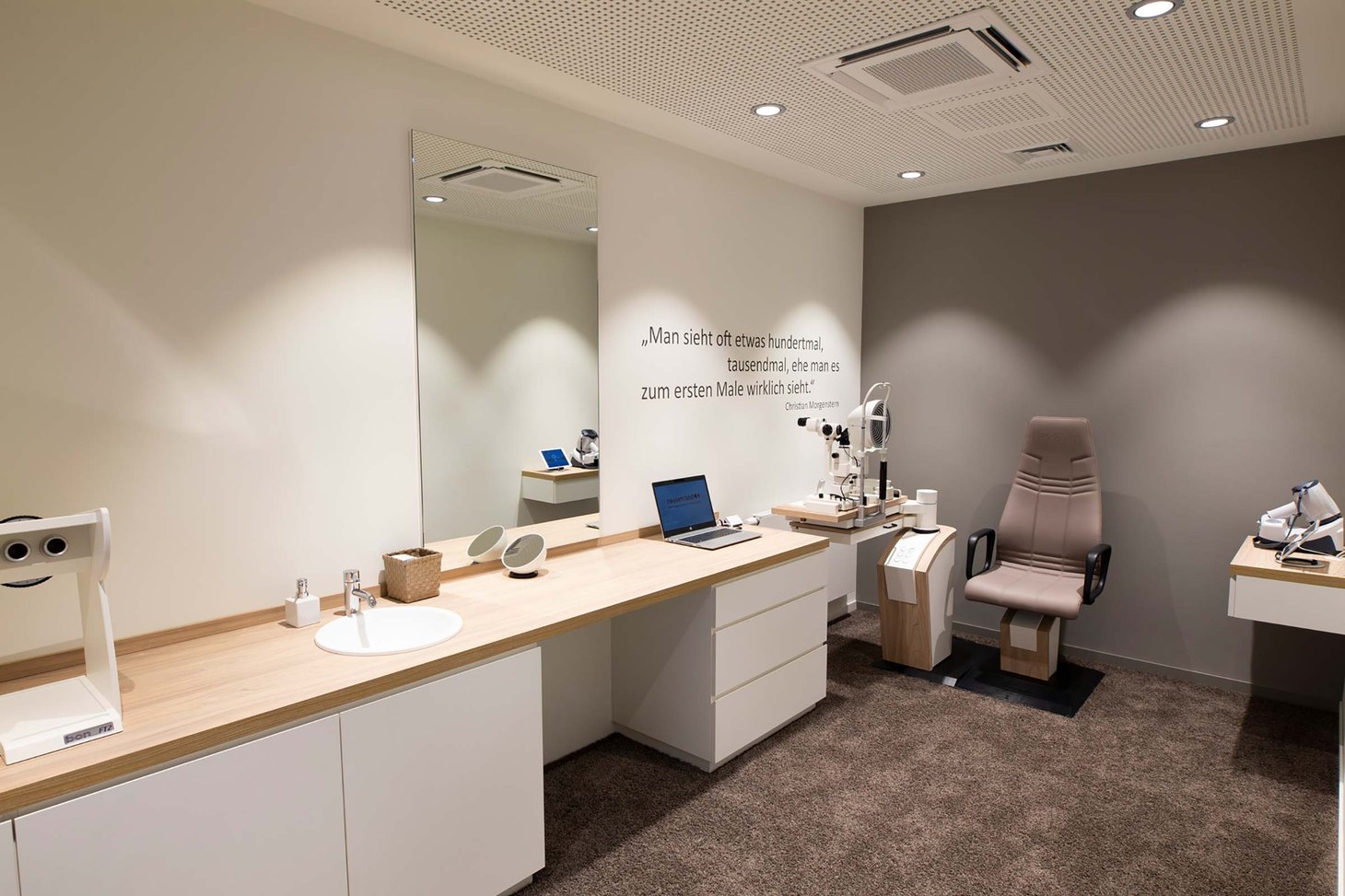 Augenoptik-Messraum mit Untersuchungsstuhl, Geräten und Zitat an der Wand, Waschbecken seitlich