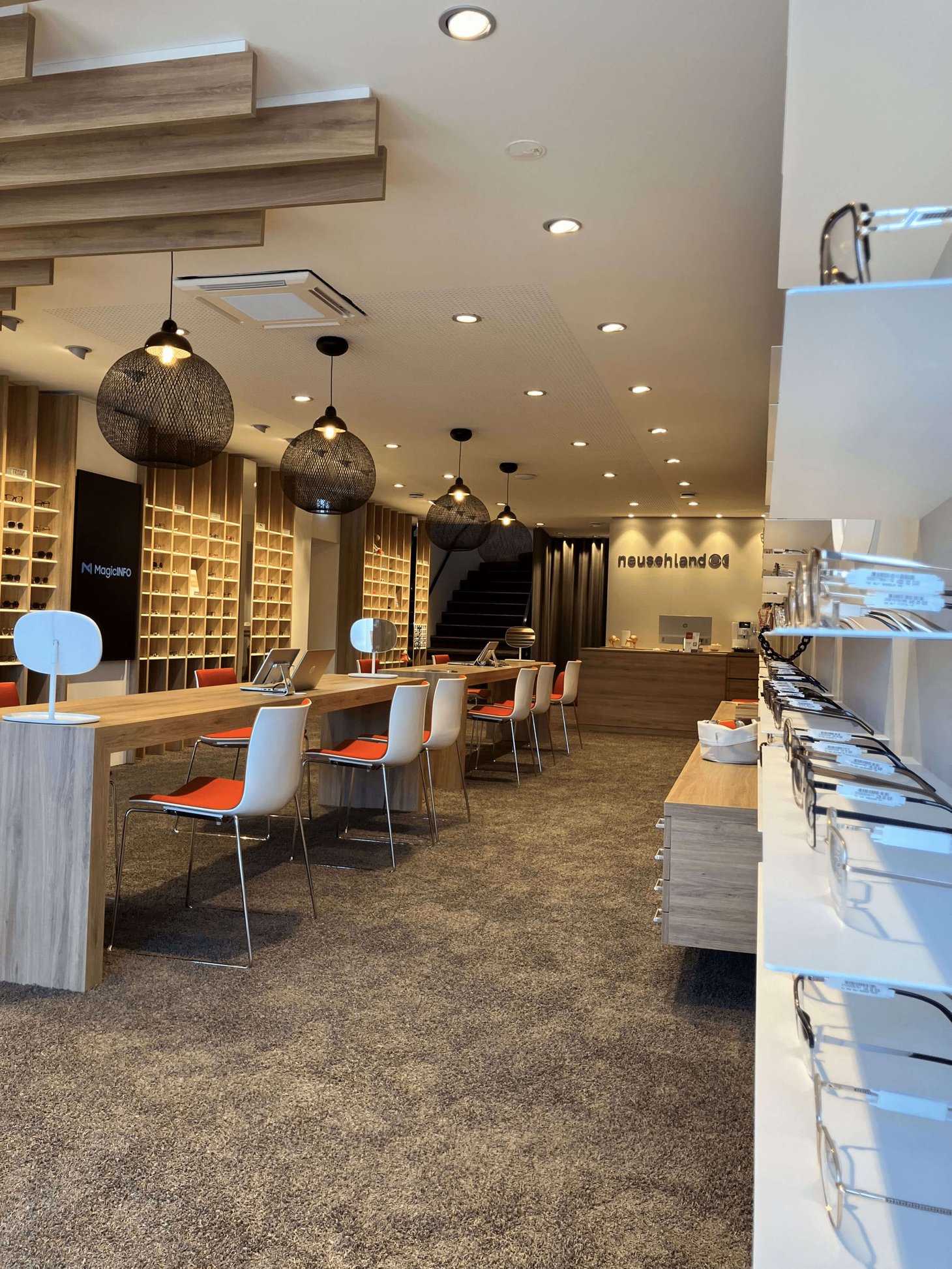 Weitläufiger Optikerverkaufsraum mit Hängeleuchten, Beratungstischen und Brillenregalen rechts