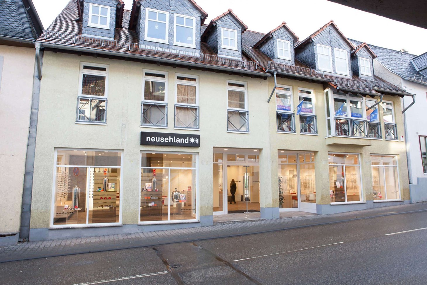 Ladenfront mit Schriftzug "neusehland" in einer Innenstadt, mehrere Schaufenster, Wohnhaus darüber