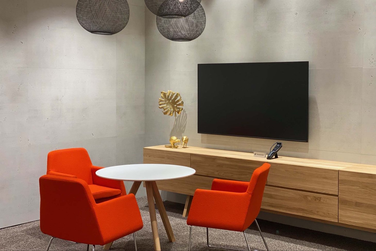 Zwei orangefarbene Sessel und runder Tisch vor Holzsideboard mit Wandfernseher