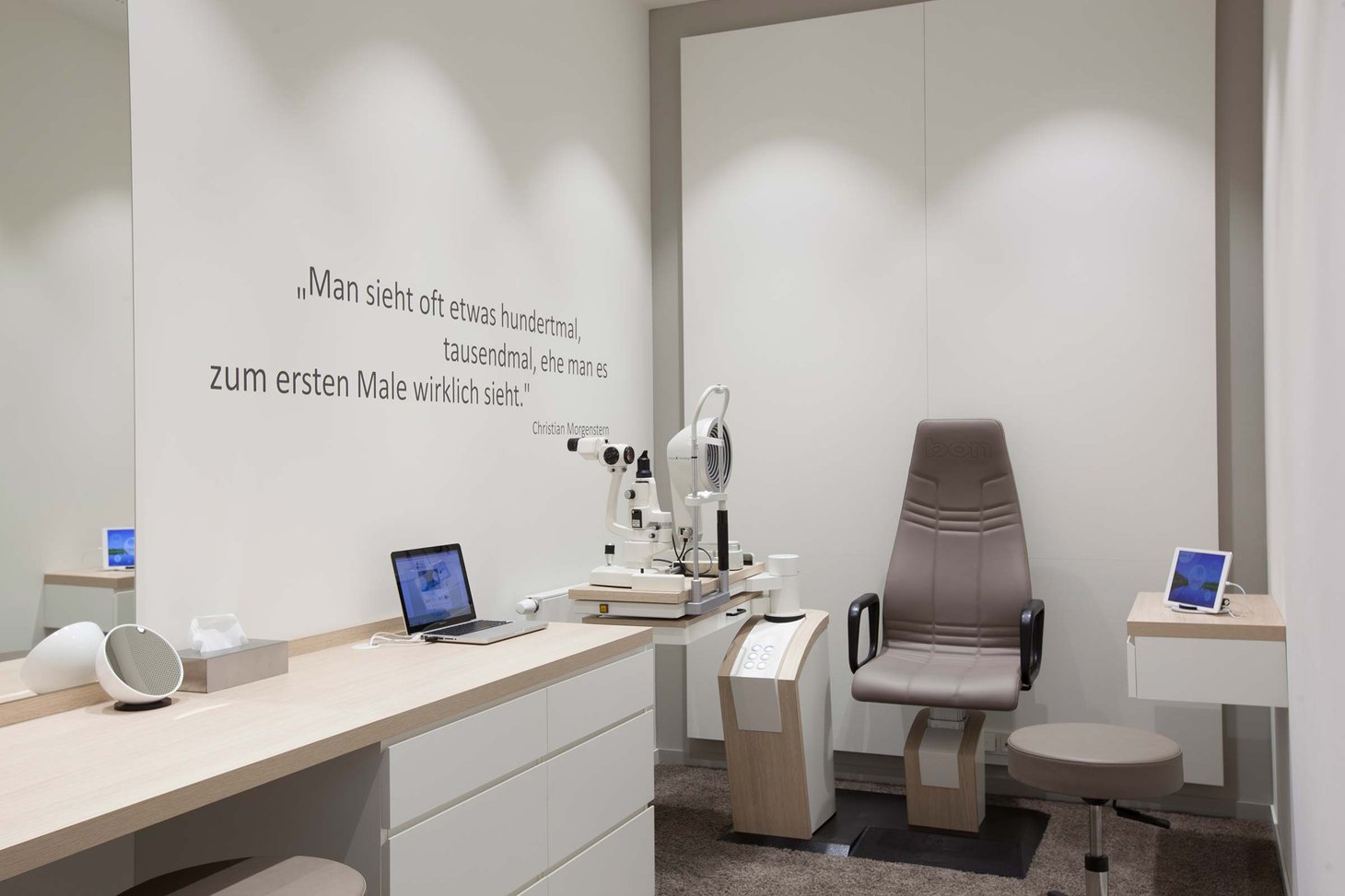 Heller Untersuchungsraum beim Optiker mit Spaltlampe, Patientenstuhl und Laptop