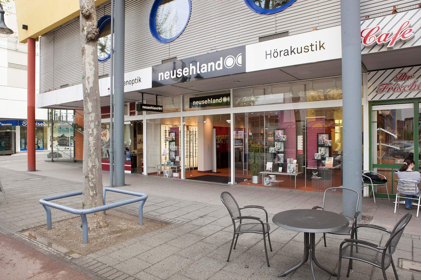 Neusehland-Filiale mit Schriftzug "neusehland" und "Hörakustik", Fußgängerzone mit Tischen