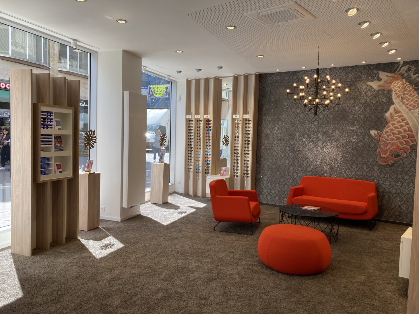 Heller Optikerverkaufsraum mit roter Sitzgruppe, Brillenregalen und gemusterter Tapete