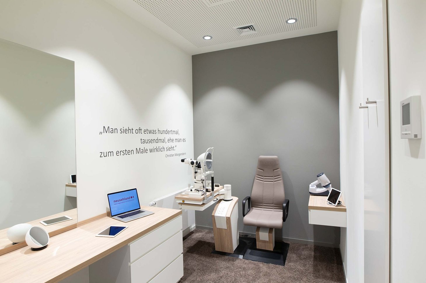 Untersuchungsraum mit Spaltlampe, Patientenstuhl, Laptop und Spiegel an der Wand