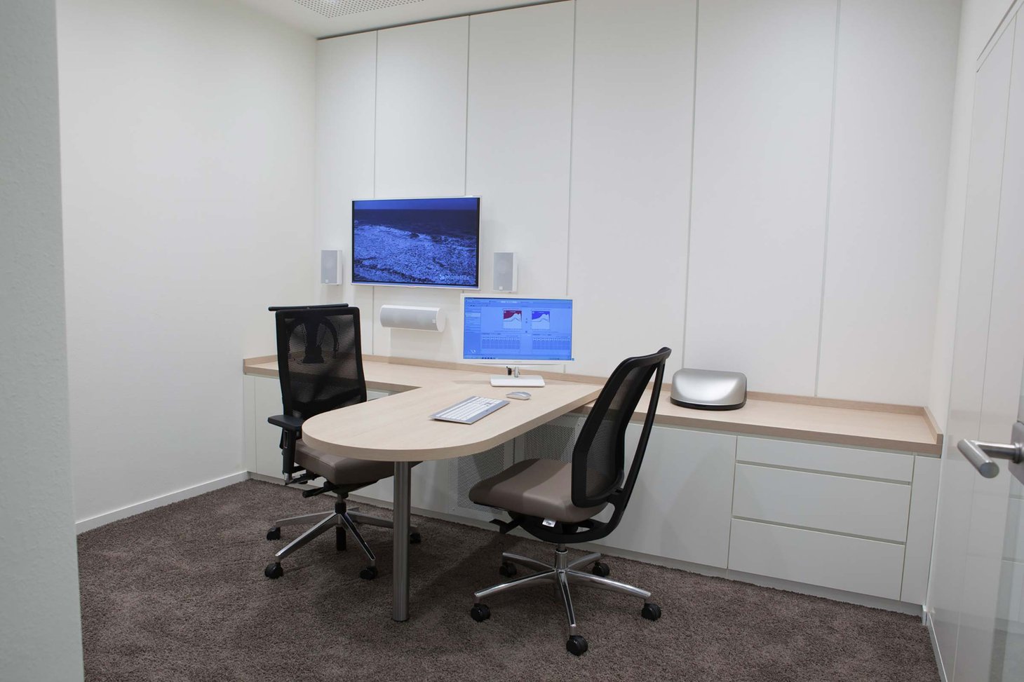 Kleiner Beratungsraum mit rundem Tisch, zwei Bürostühlen, Monitor und Wandbildschirm