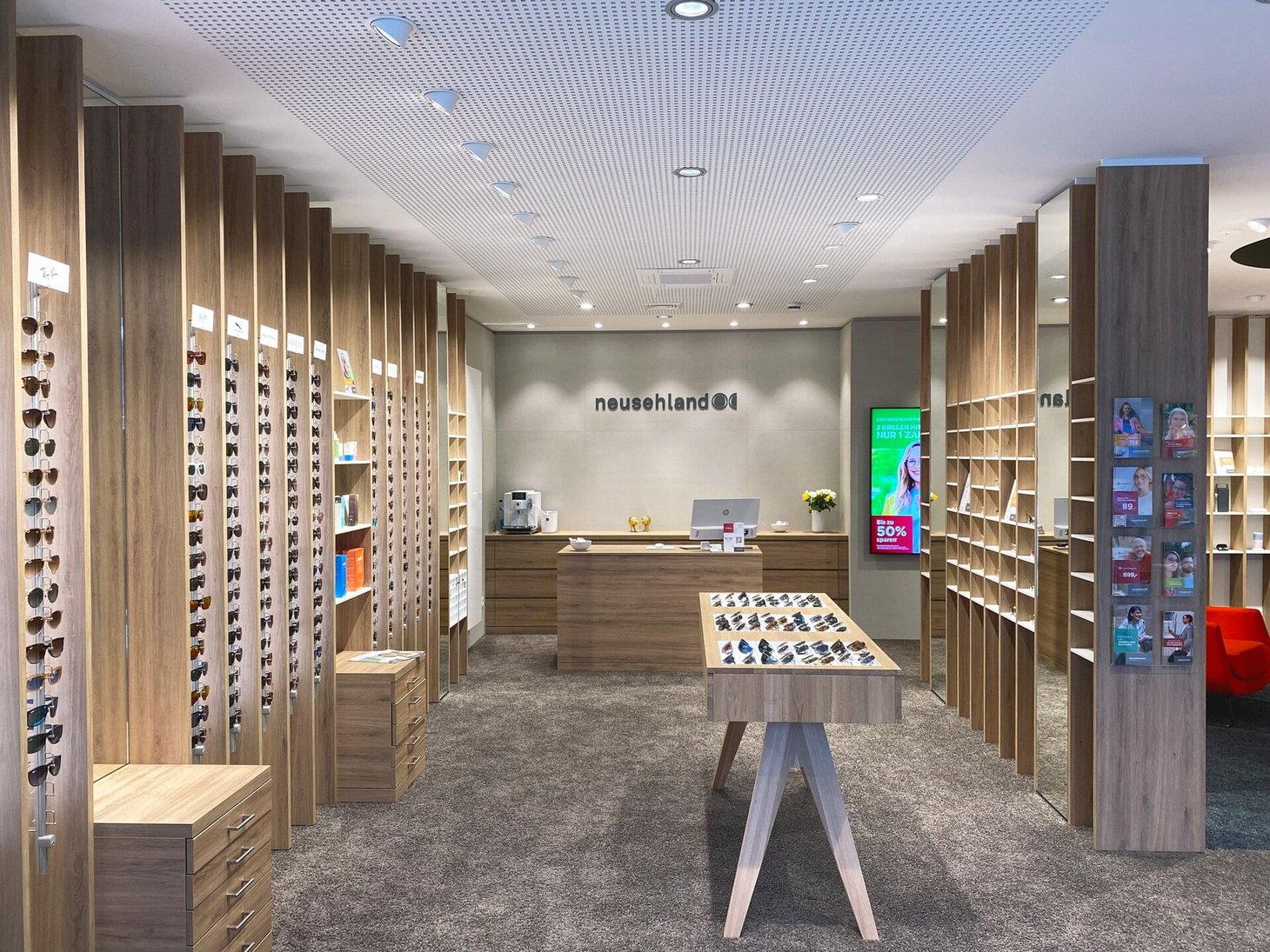 Optiker-Innenraum mit Holzregalen, Empfangstheke und Schriftzug "neusehland" an der Rückwand