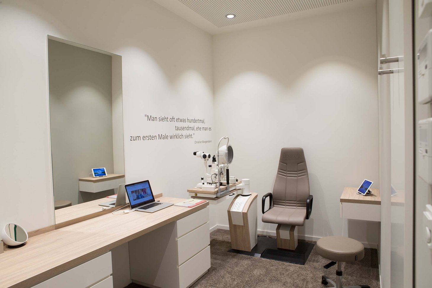 Untersuchungsraum mit Spaltlampe, Patientenstuhl, Laptop und Spiegel an der Wand