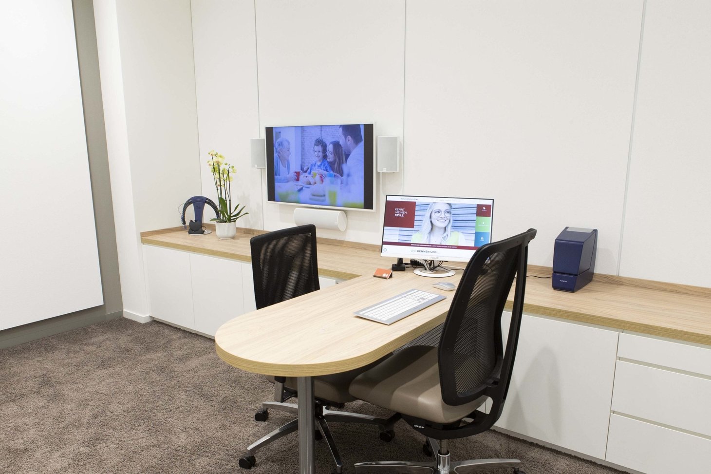 Kleiner Beratungsraum mit rundem Tisch, zwei Bürostühlen, Monitor und Wandbildschirm