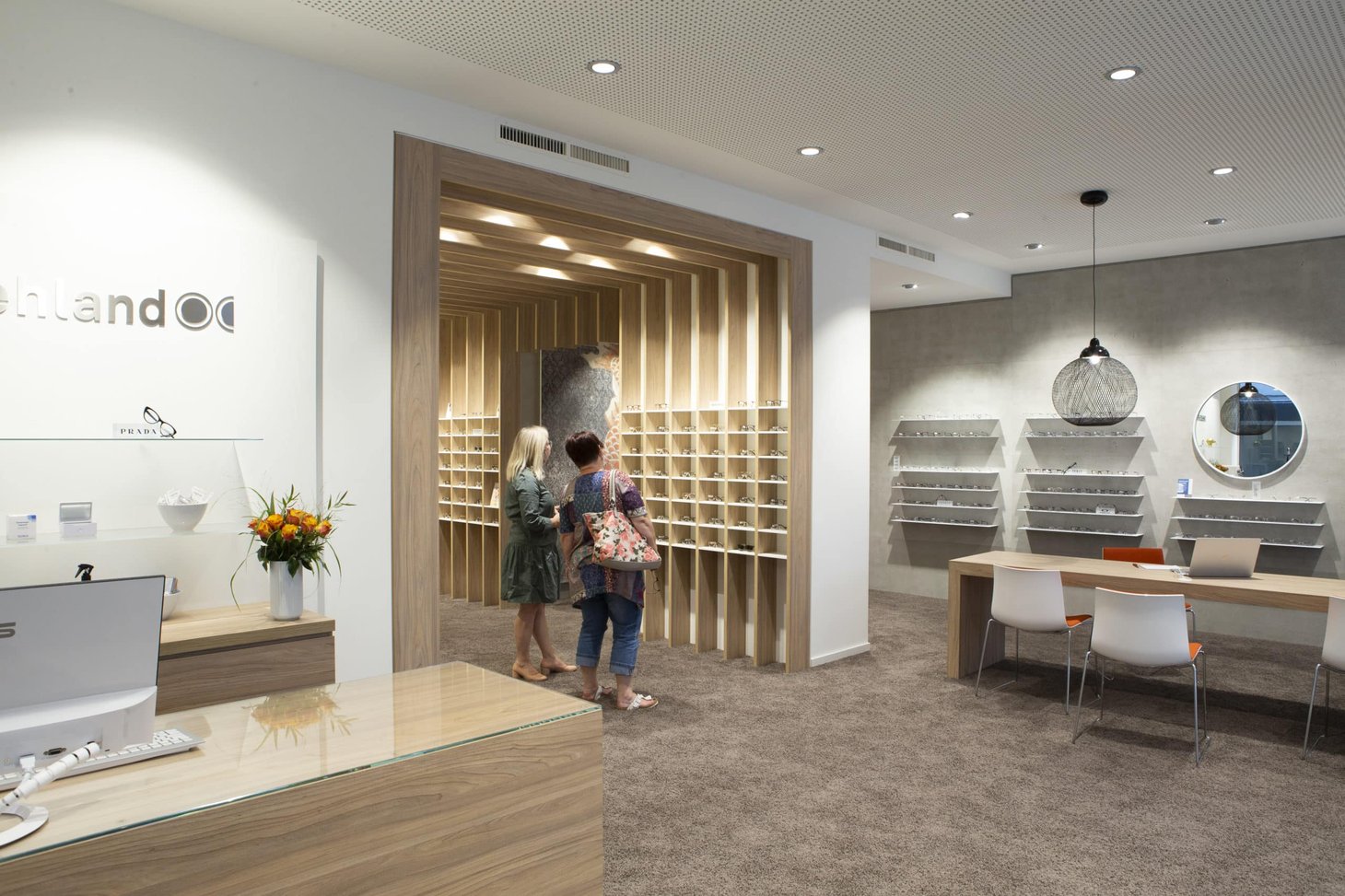 Zwei Frauen stehen im Optiker-Geschäft vor einem Brillenregal aus hellem Holz