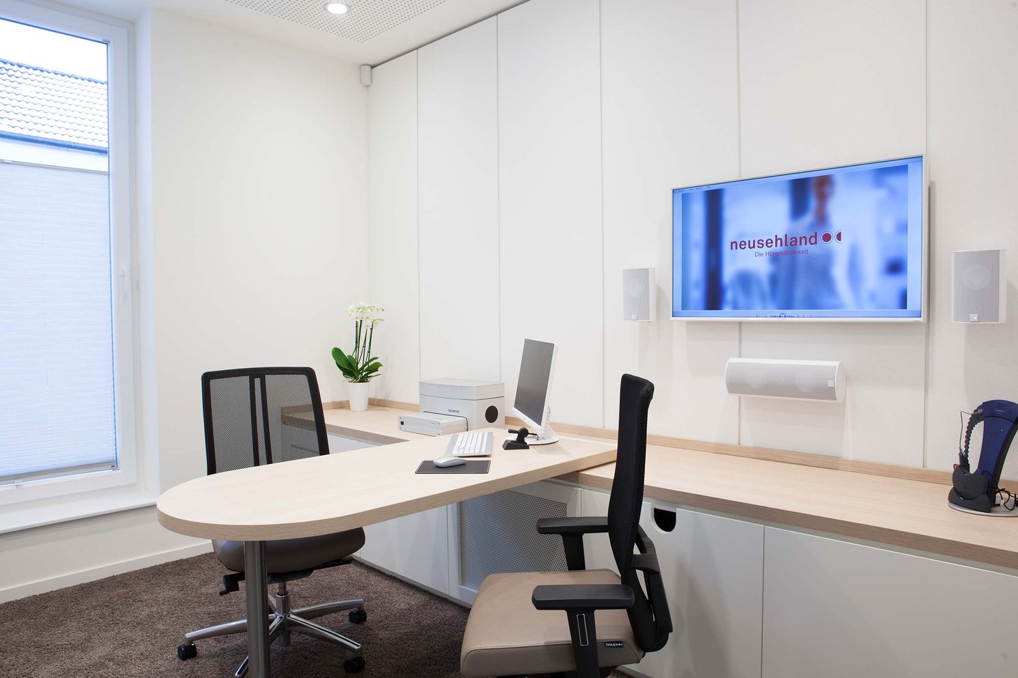 Kleiner Beratungsraum mit rundem Tisch, zwei Bürostühlen, Monitor und Wandbildschirm