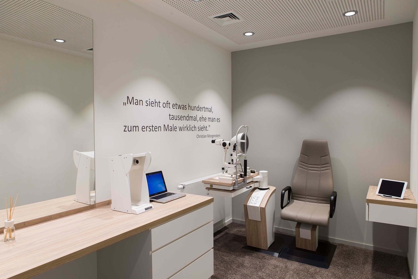 Untersuchungsraum mit Spaltlampe, Patientenstuhl und Zitat von Christian Morgenstern an der Wand