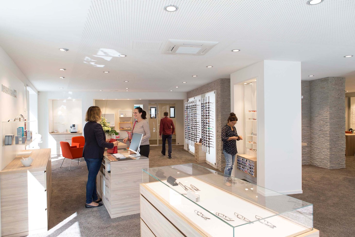Vier Personen in einem Optiker-Geschäft, zwei betrachten Brillen an der Wand