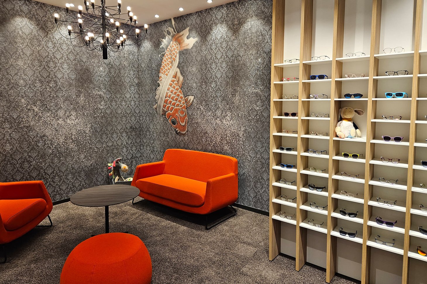 Wartebereich mit orangefarbenem Sofa, Koi-Wandbild und Brillenregal aus Holz