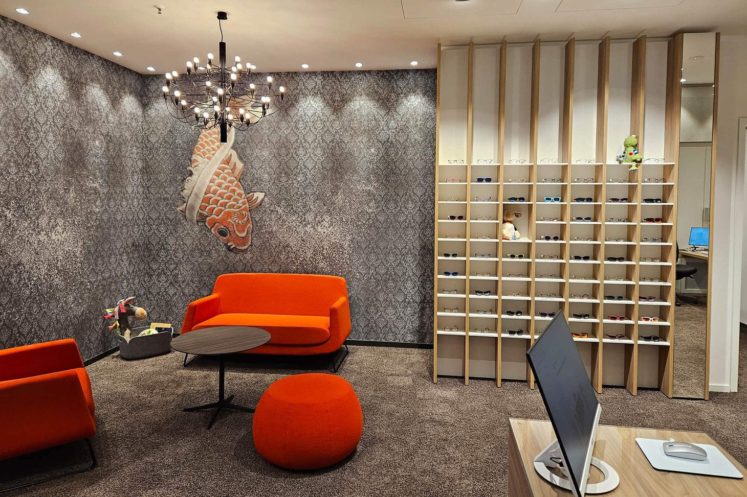 Wartebereich mit orangefarbenem Sofa, Koi-Wandbild und Brillenregal aus Holz