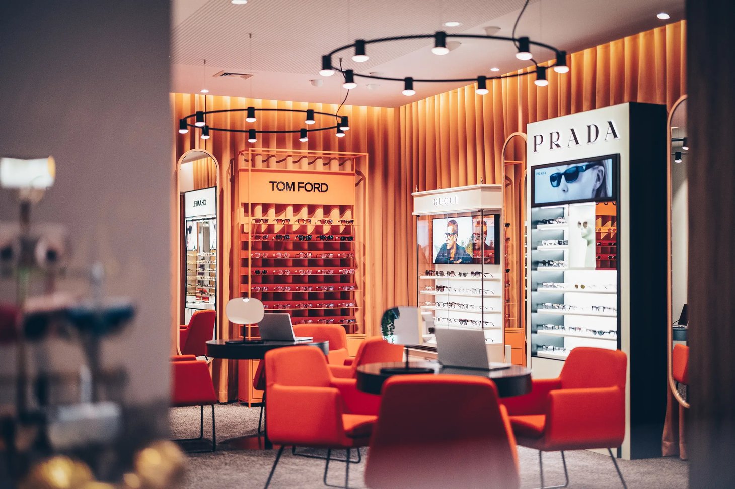 Innenraum eines Optikergeschäfts mit Brillenregalen und Markenbereichen Tom Ford, Prada und Gucci.