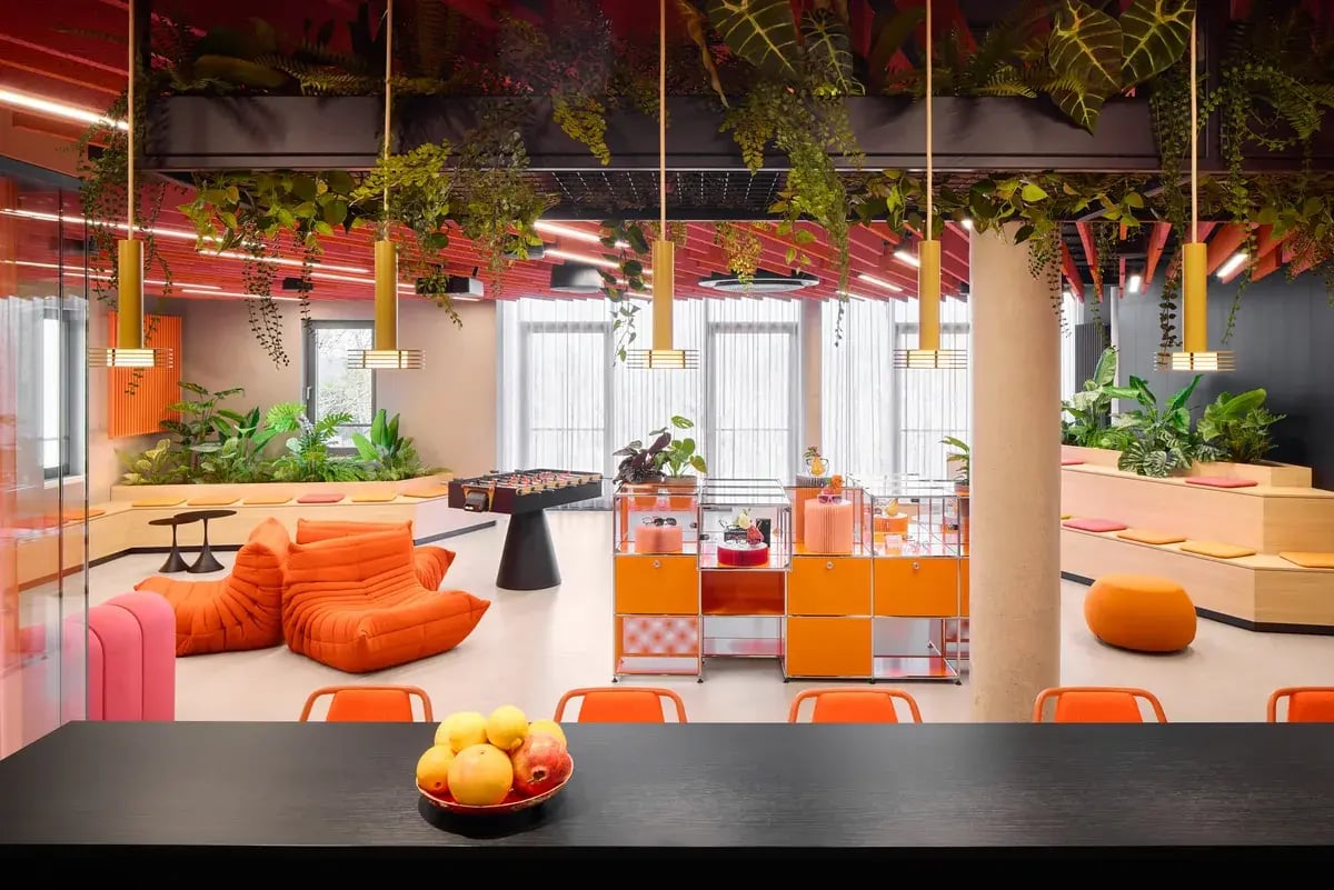 Gemeinschaftsraum mit orangefarbenen Sesseln und Zimmerpflanzen.