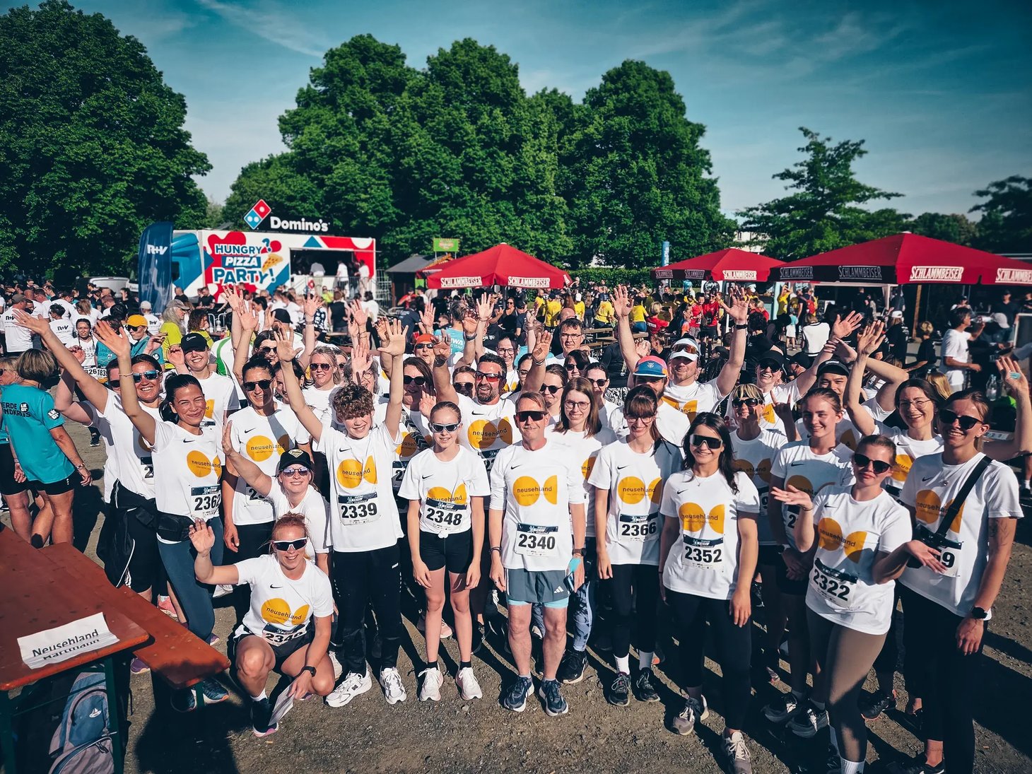 Große Gruppe in weißen T-Shirts jubelt beim Start eines Laufevents im Freien.