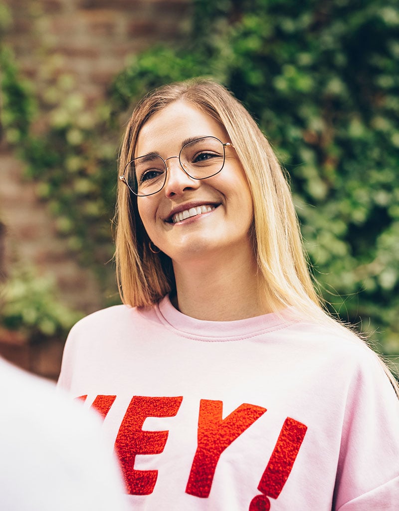 Frau mit Brille vor unscharfem Hintergrund im Freien.