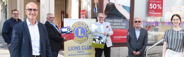 Mann mit Karton voller Hörgeräte vor einem Lions-Club-Schild