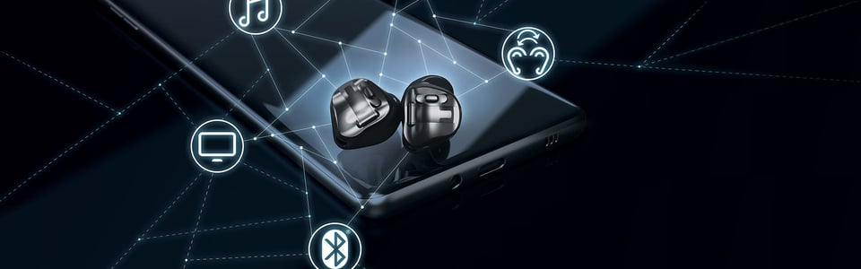 Hörgeräte liegen auf einem Smartphone mit Symbolen für Bluetooth und moderne Hörtechnologie